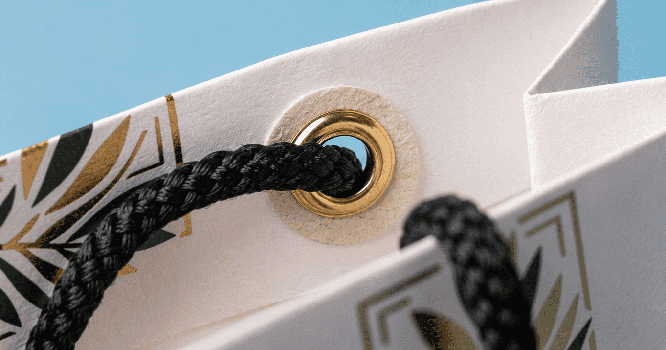 Custom paper bag printing in Singapore showing a close-up of a luxury paper bag with black rope handles, gold eyelet reinforcement, and premium foil-printed details for durable retail packaging.